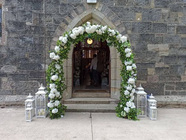 "Large artificial floral arch positioned at the entrance of a church, part of Evergreen Silk Plants’ Enchanted Package."