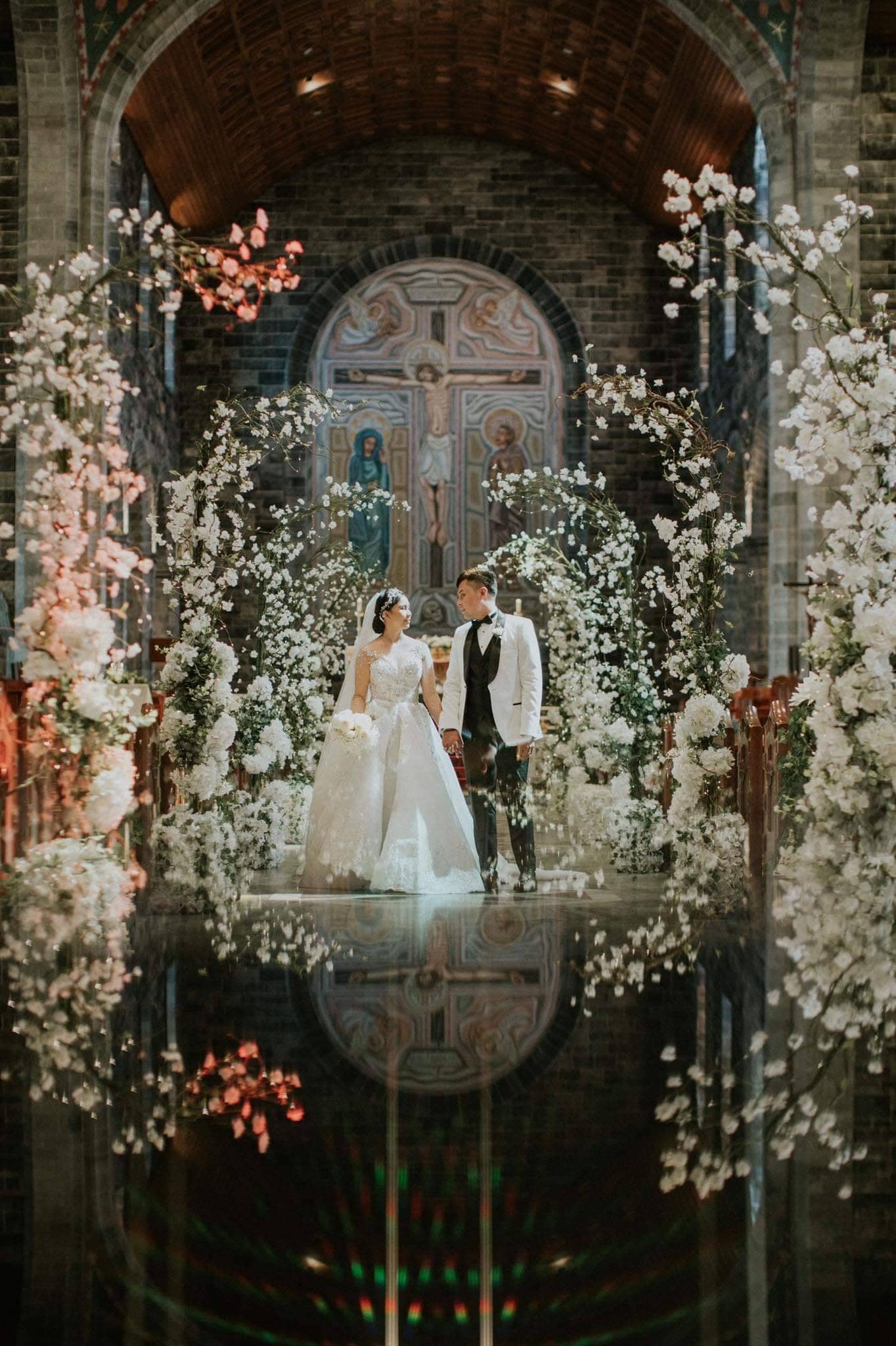 "Bride and groom walking down an aisle framed by enchanted light-up tree arches from Evergreen Silk Plants."