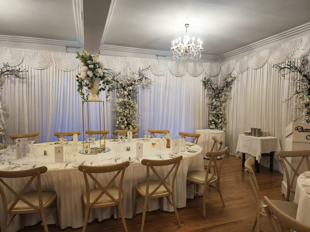Full wedding reception table styling with white draping and tall floral stand decor