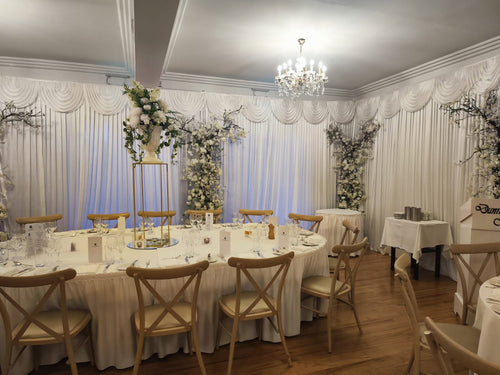 Full wedding reception table styling with white draping and tall floral stand decor