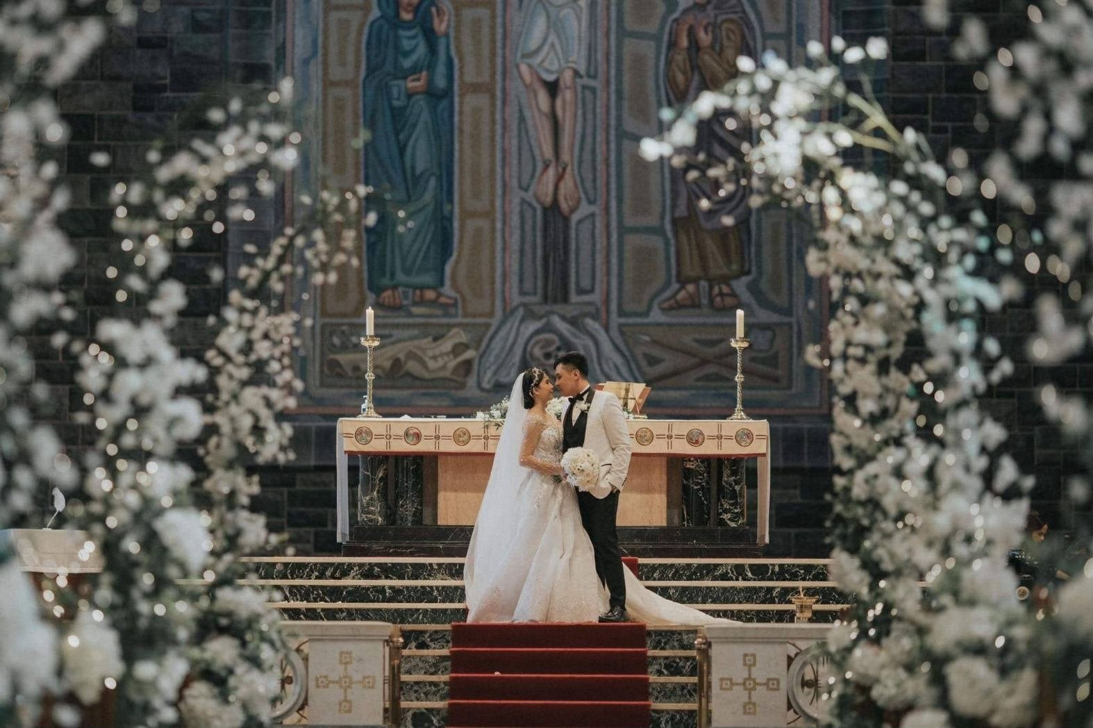 Bride and groom kissing at the altar framed by white blossom wedding arches