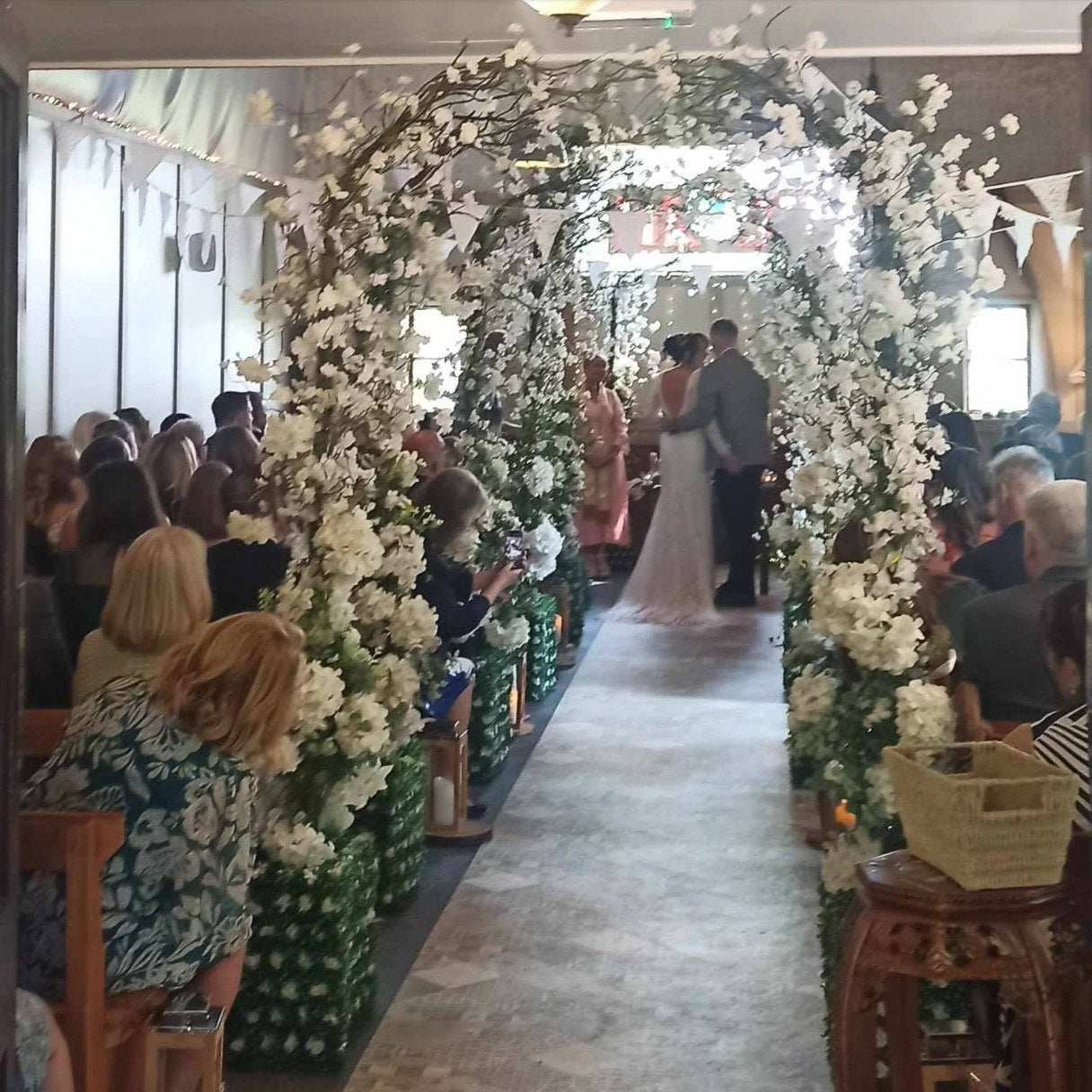 Bride and groom at the top of a church aisle framed by floral wedding arches