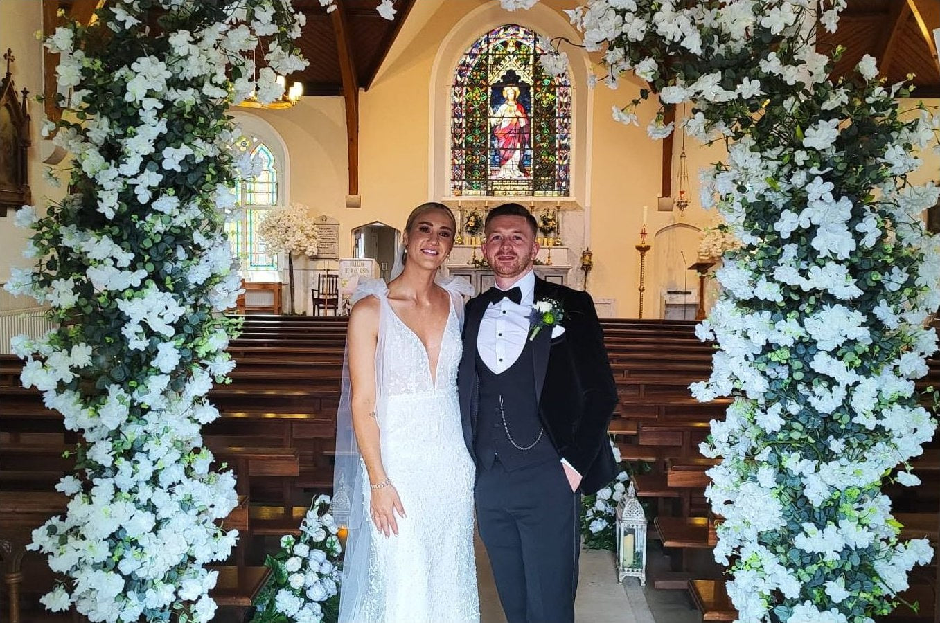 Bride and groom smiling in a church framed by white floral wedding decor
