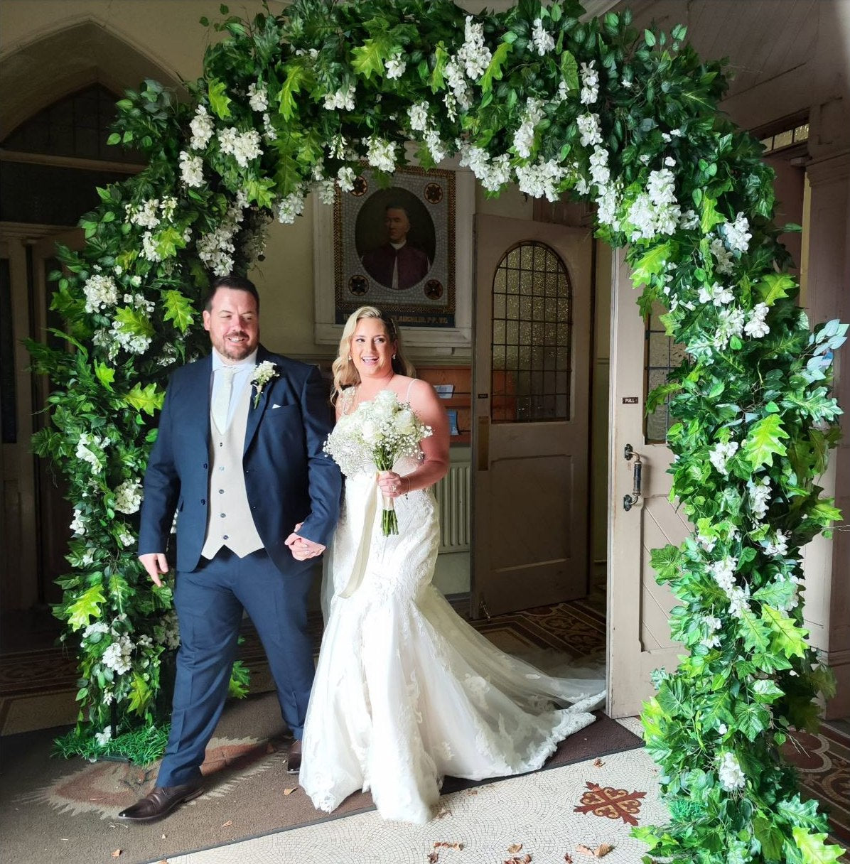 Bride and groom standing under a green and white wedding doorway arch