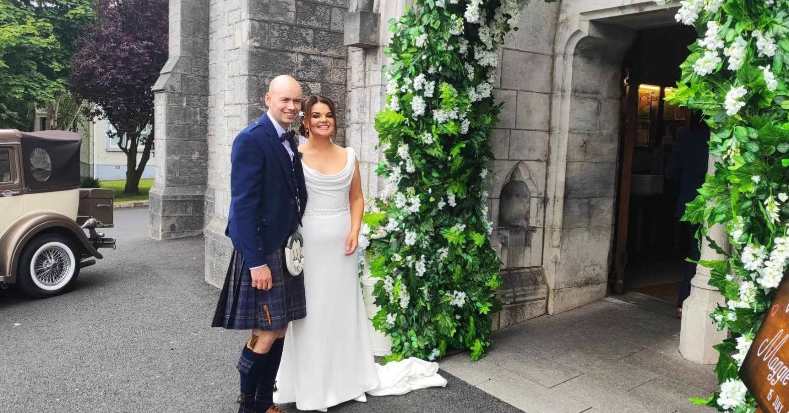 Bride and groom outside a stone church entrance with a green floral doorway arch