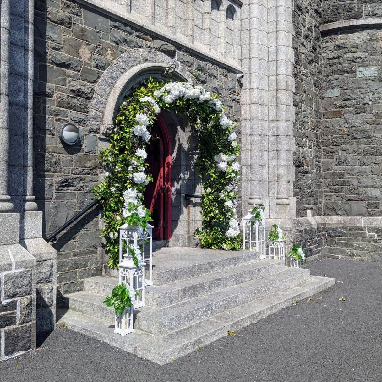 Bride and groom on stone church steps with white floral entrance styling
